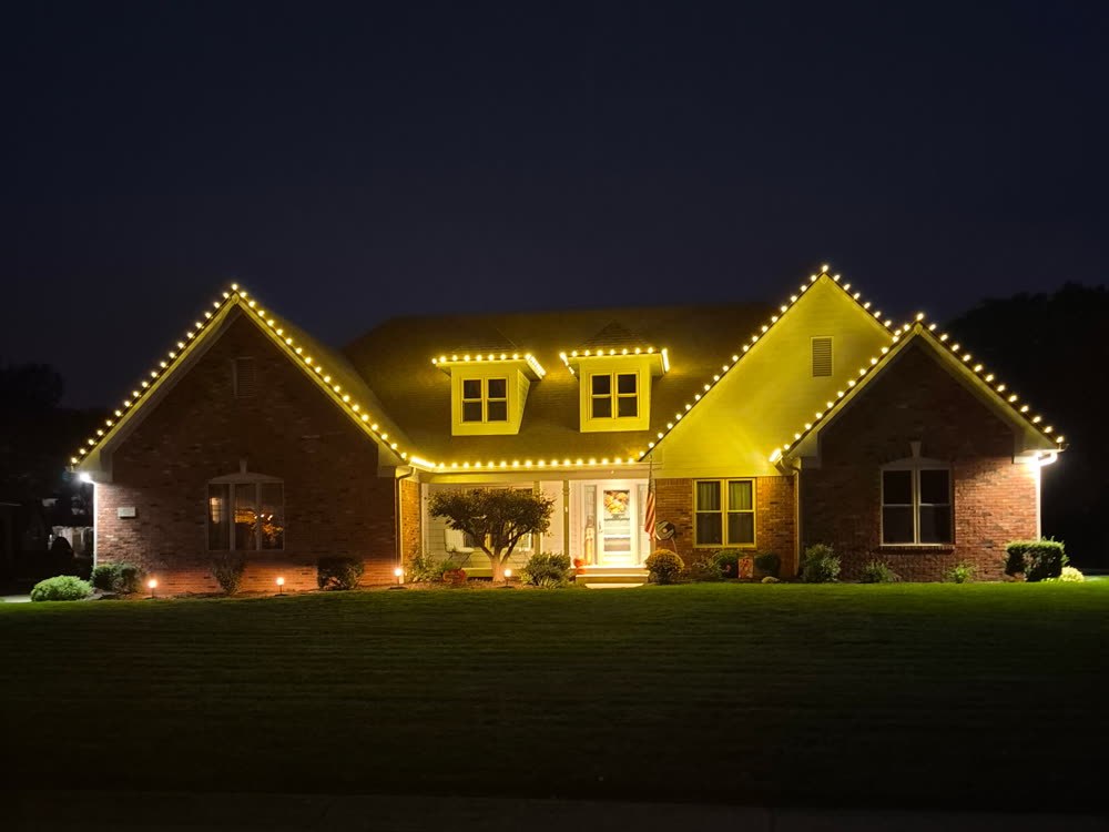 Brick home with triple gables lined in warm white Christmas lights