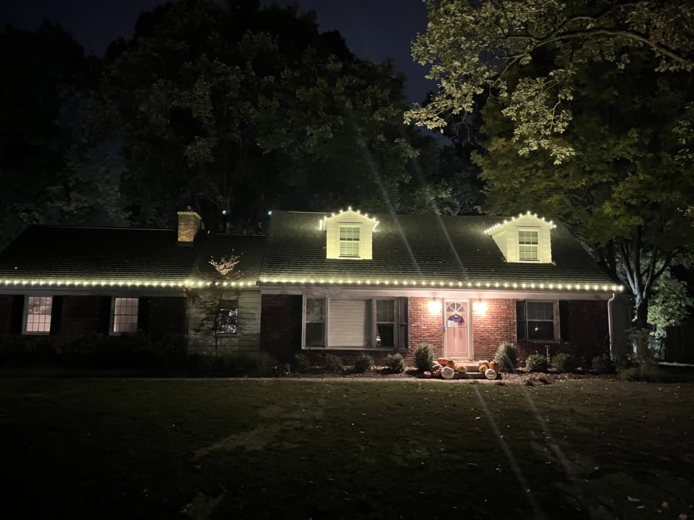 Ranch home with dormers and warm white Christmas lights along the full roofline