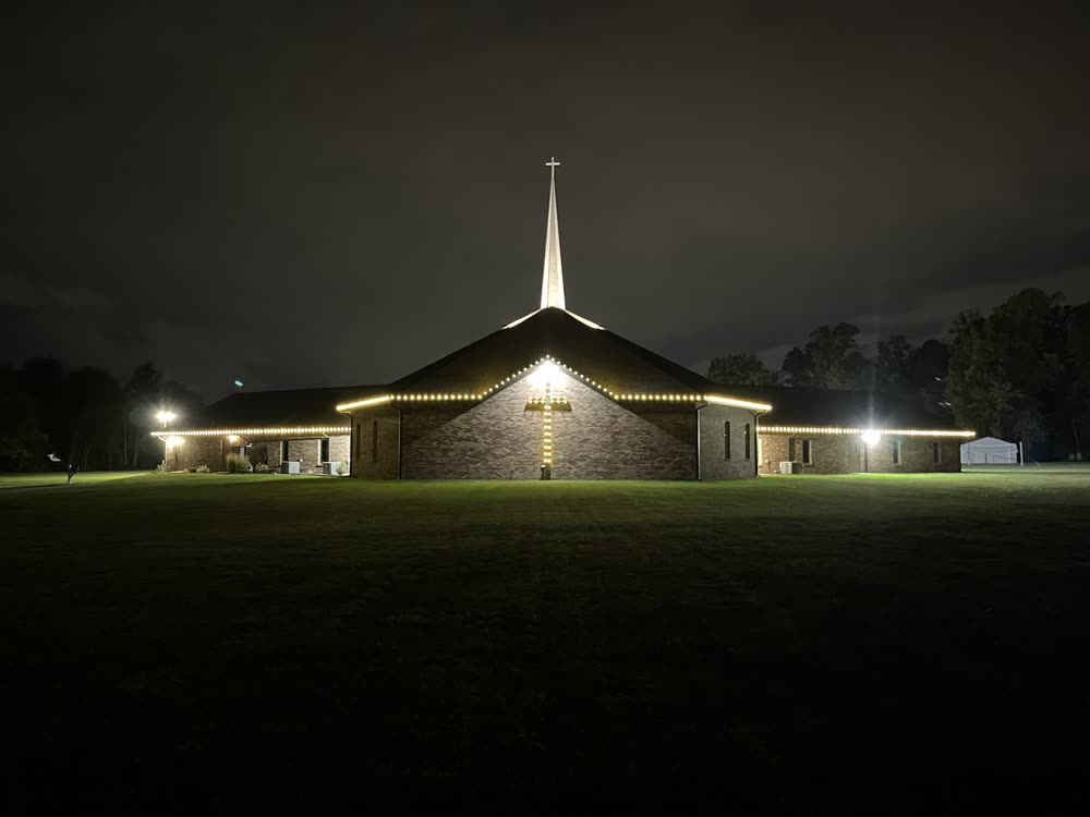 Church with warm white Christmas lights along the roofline and a lit steeple