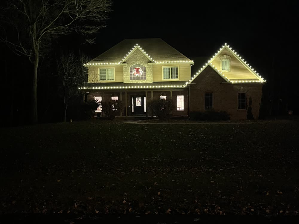 Two-story home with a wreath and warm white Christmas lights along the roofline