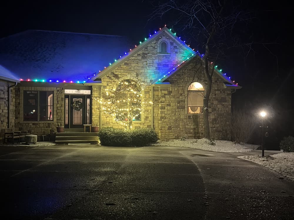 Stone home with custom multicolor Christmas lights along the roofline
