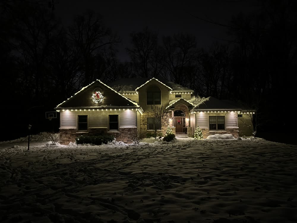 Home with warm white roofline Christmas lights and fresh snow on the ground