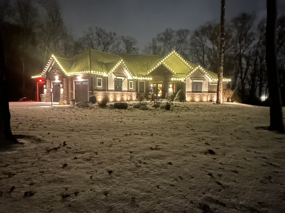 Long ranch home with warm white Christmas lights along the roofline in the snow