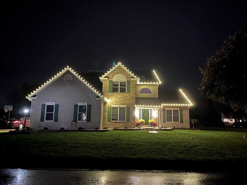 Two-story home with warm white Christmas lights outlining every peak