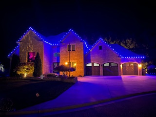 Large brick home with custom blue Christmas lights along roofline and garage