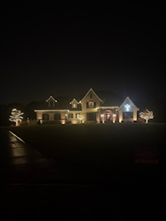 Large estate home with warm white roofline lights and wrapped trees